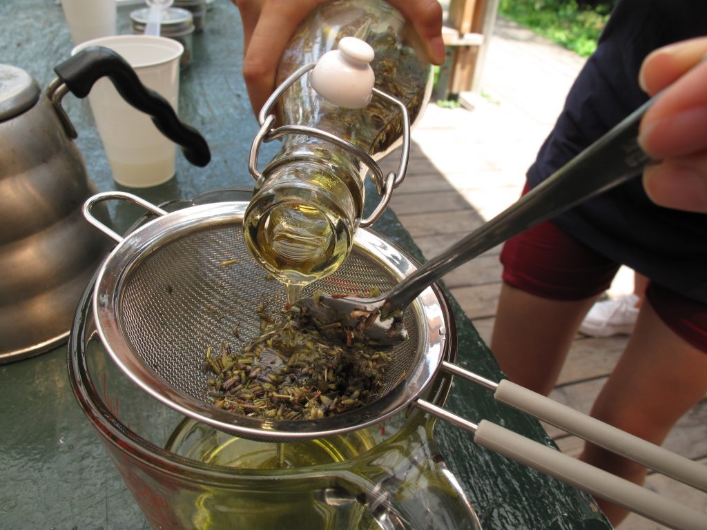 Close up of hands pouring a jar of oil and herbs through a small sieve